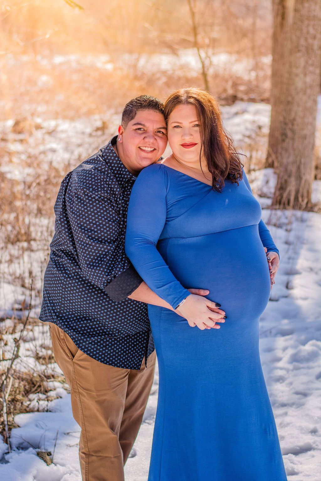 Couple posing in winter snow, with one wearing a blue dress and the other a dark shirt and tan pants.