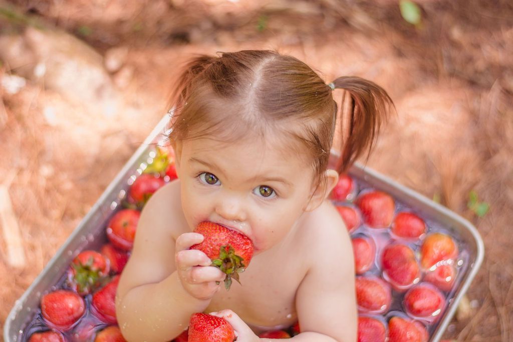 Child eating a strawberry in a basket of ripe strawberries outdoors
