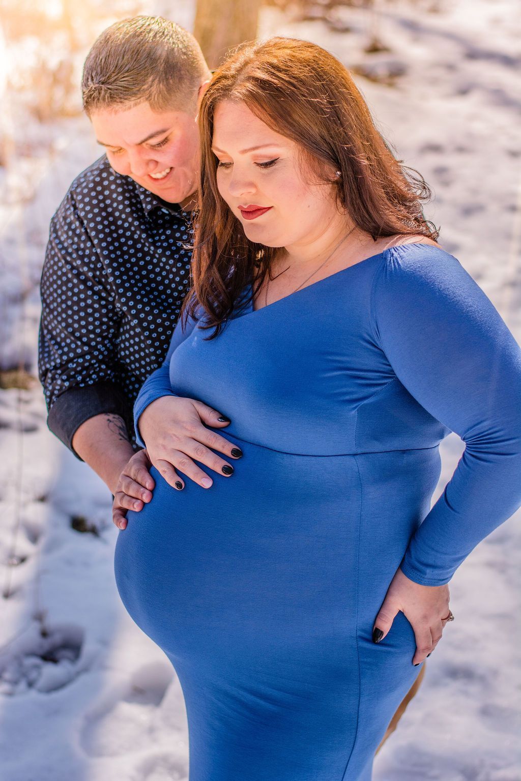 Two people outdoors in snow, embracing one wearing a blue dress, the other in a dark polka-dot shirt.