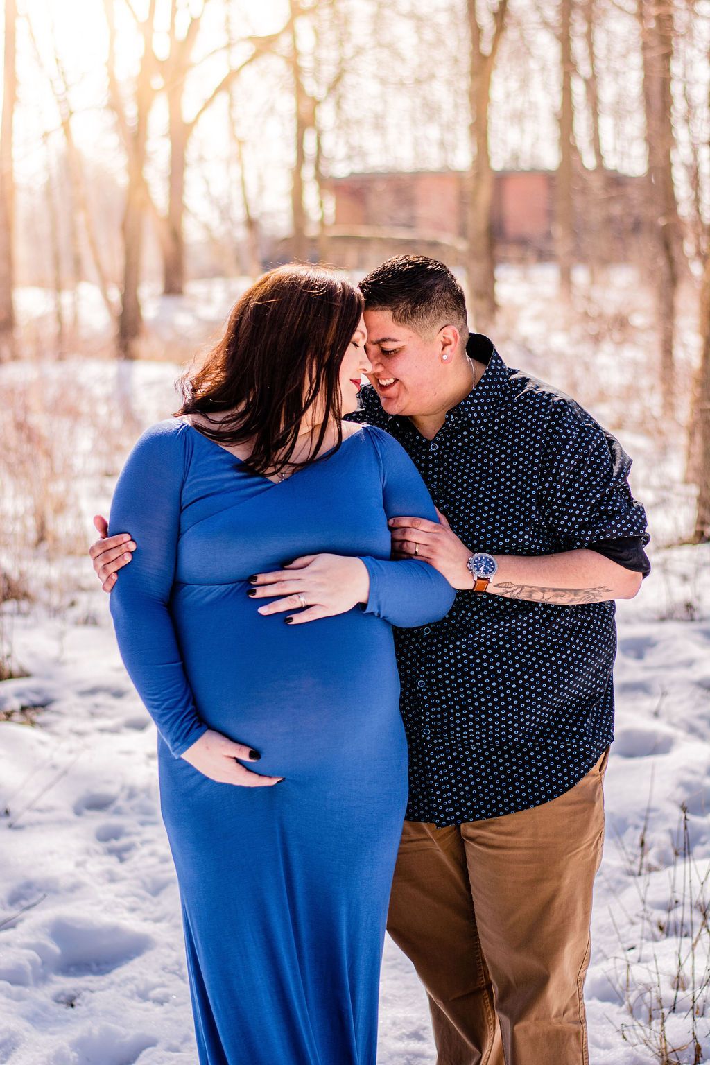Couple embracing outdoors in a snowy park, with a woman in a blue dress and a man in a dark shirt.