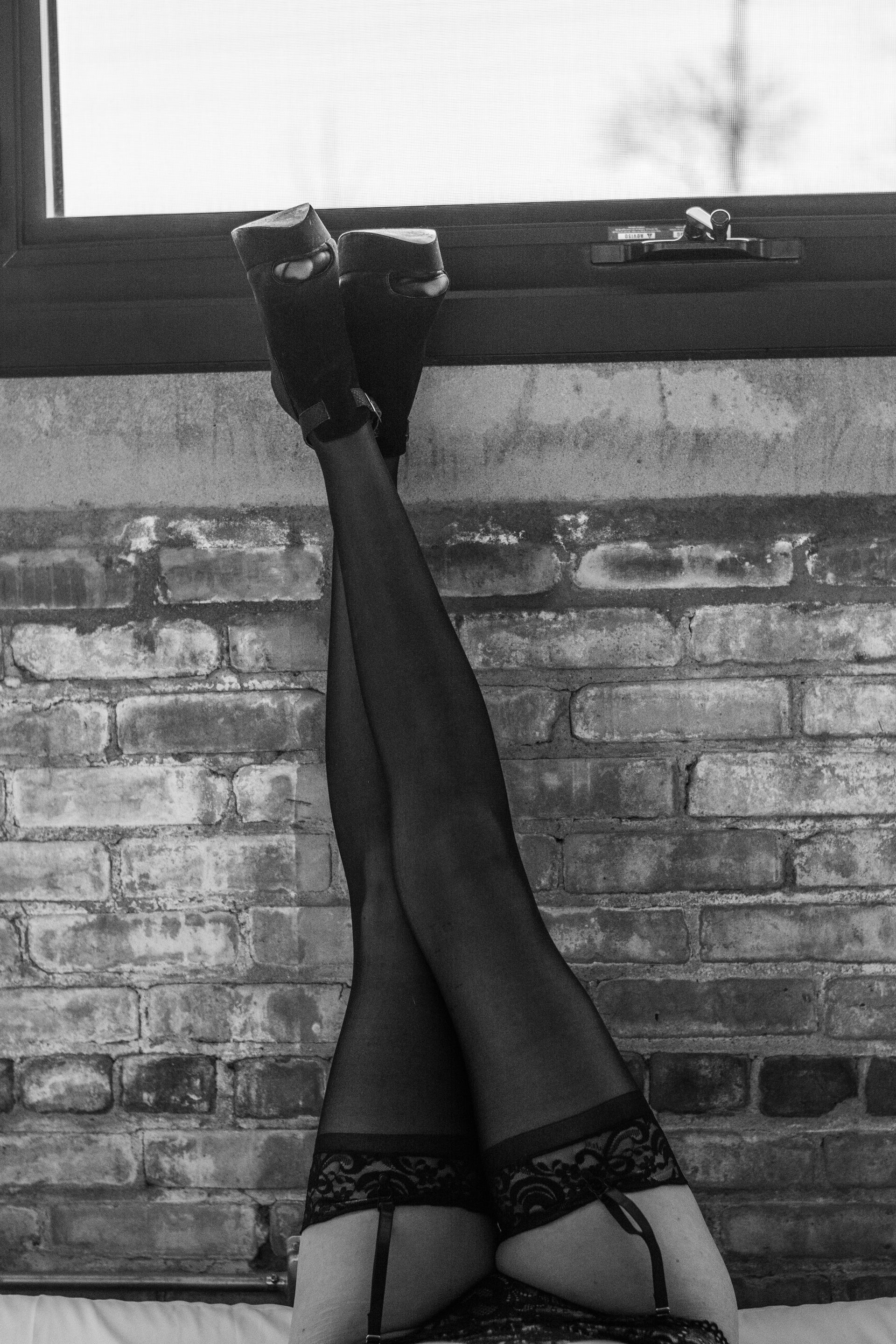 Black-and-white photo of legs in stockings resting vertically against a brick wall and window ledge