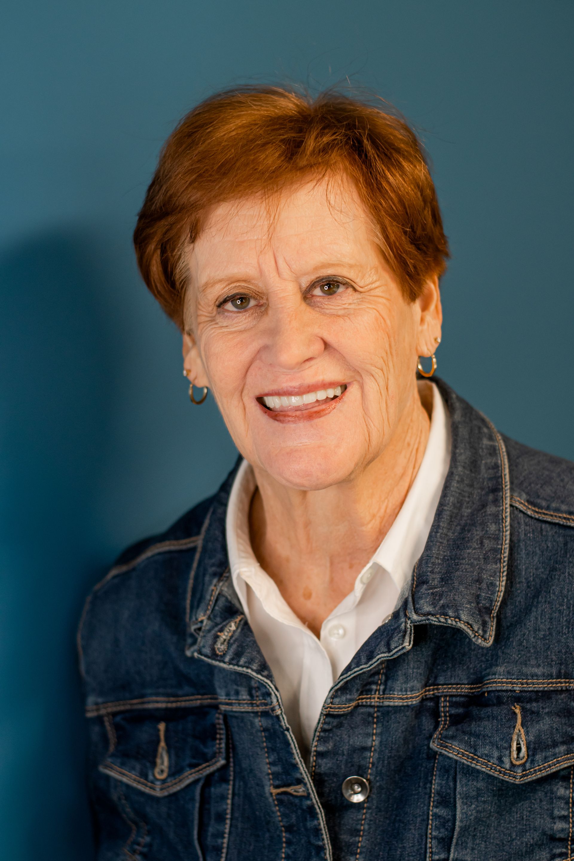 Smiling person in a denim jacket and white shirt against a blue background
