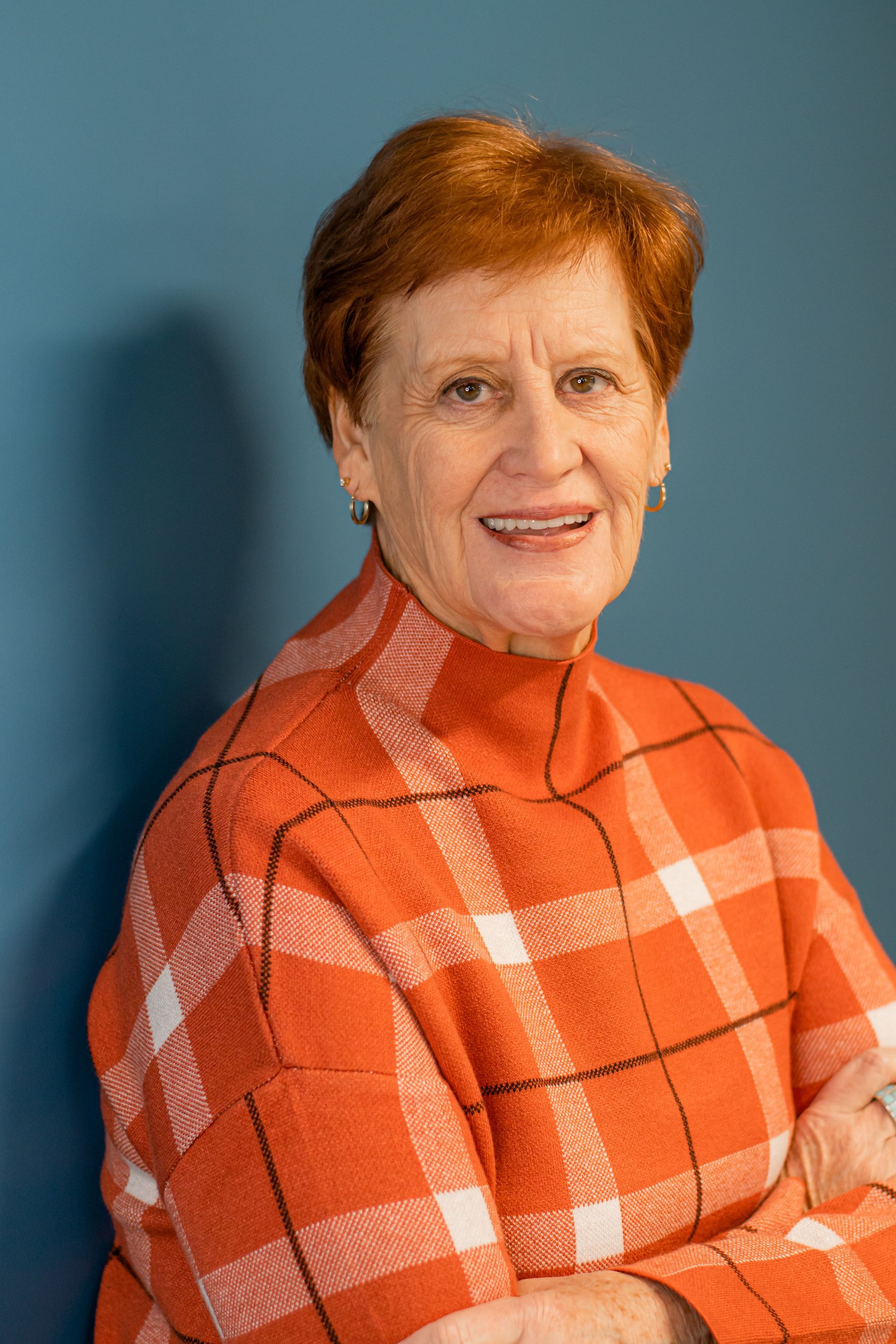 Portrait of a smiling woman in an orange plaid sweater against a blue background