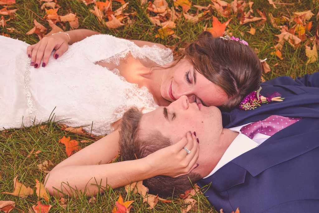Bride and groom lying on autumn leaves, touching foreheads and smiling softly
