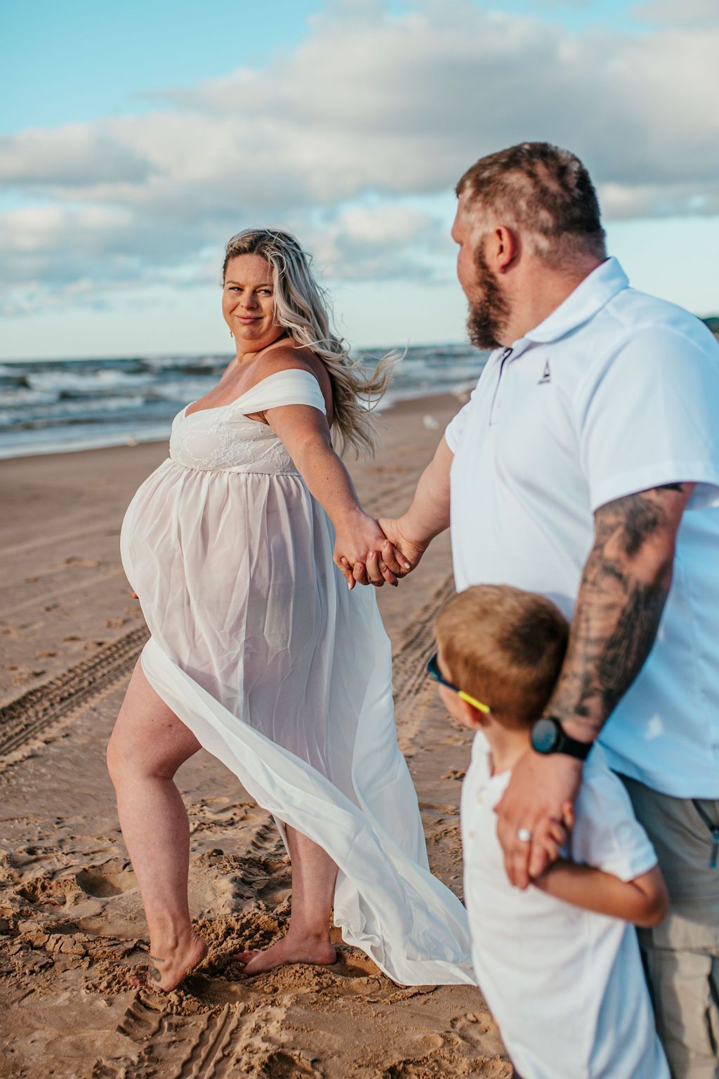 Family walking barefoot on a beach at sunset, holding hands with a child beside them.