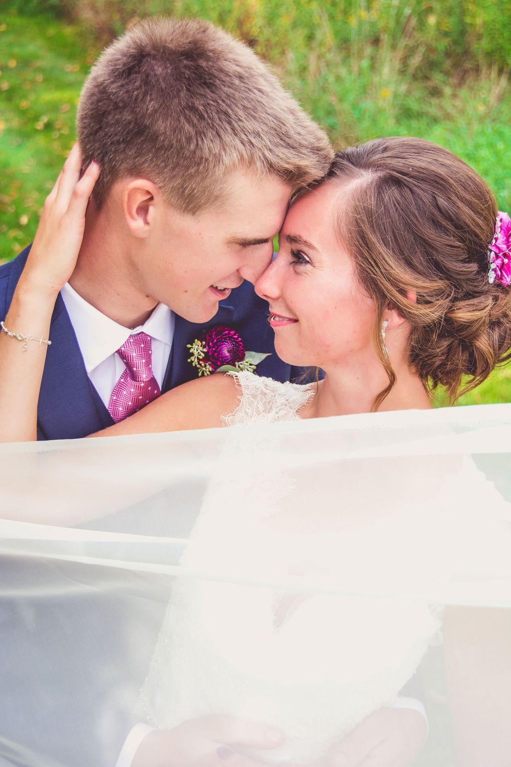 Bride and groom touching foreheads outdoors, smiling in a close wedding portrait