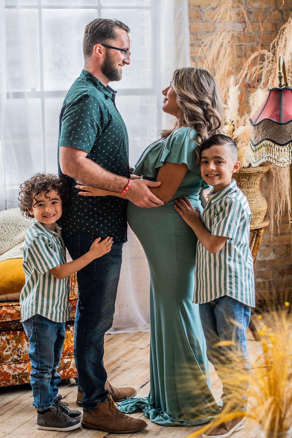 Family of four standing together indoors, with parents holding hands and two children smiling beside them.