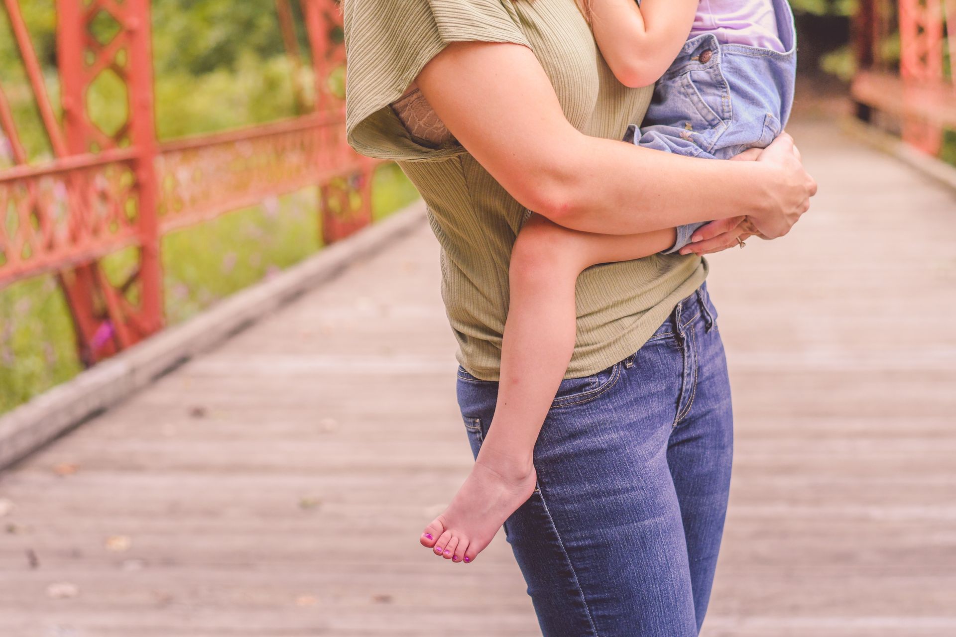 Adult carrying a child on a wooden bridge with red railings