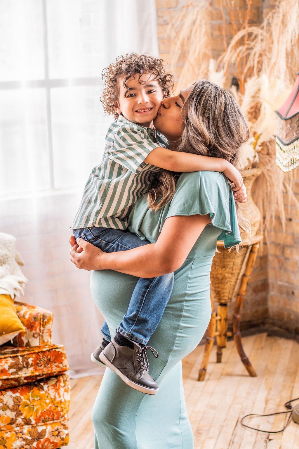 Woman holding and kissing a smiling child in a bright indoor room