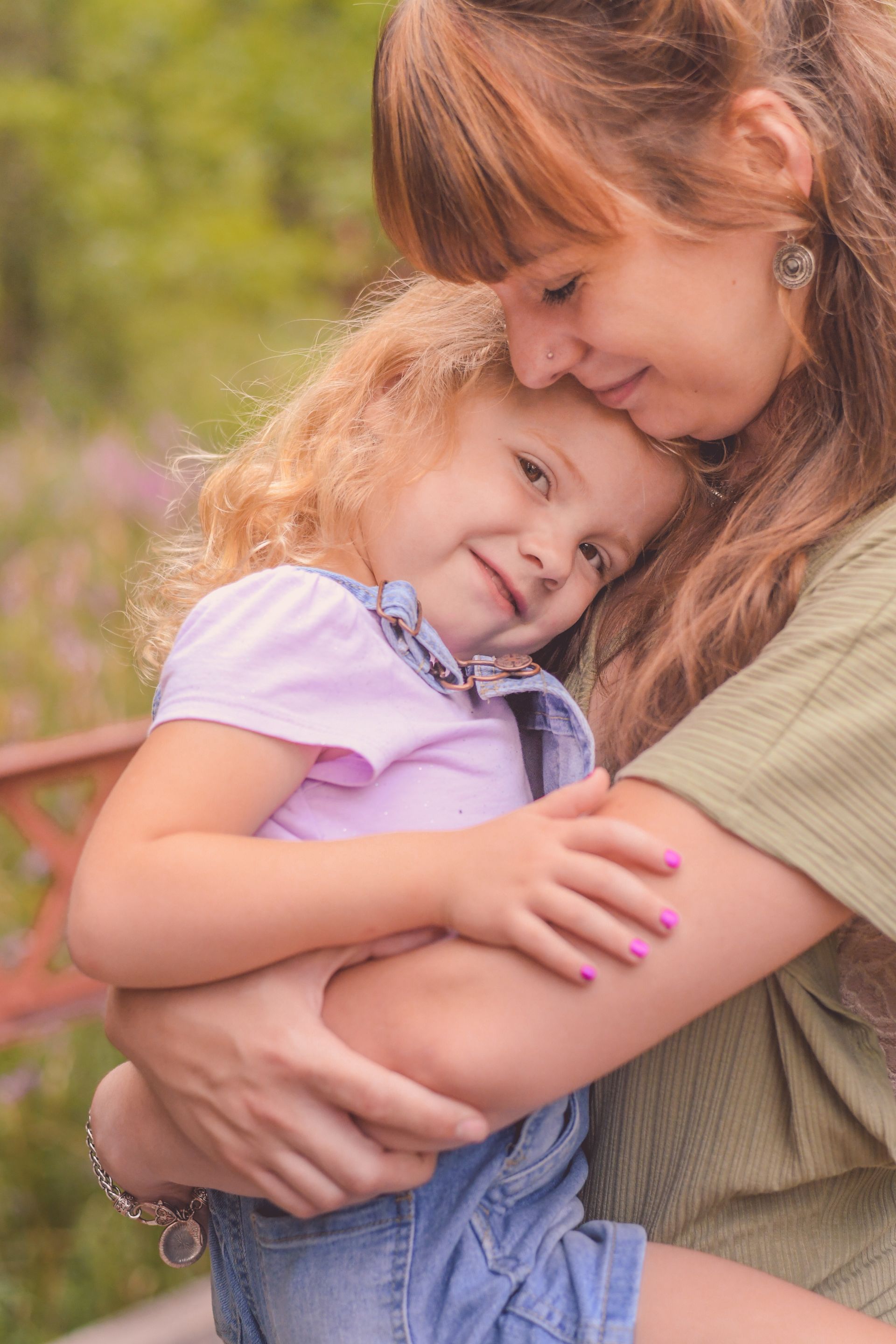 Woman holding a smiling child outdoors, both in casual clothes, with a soft blurred background
