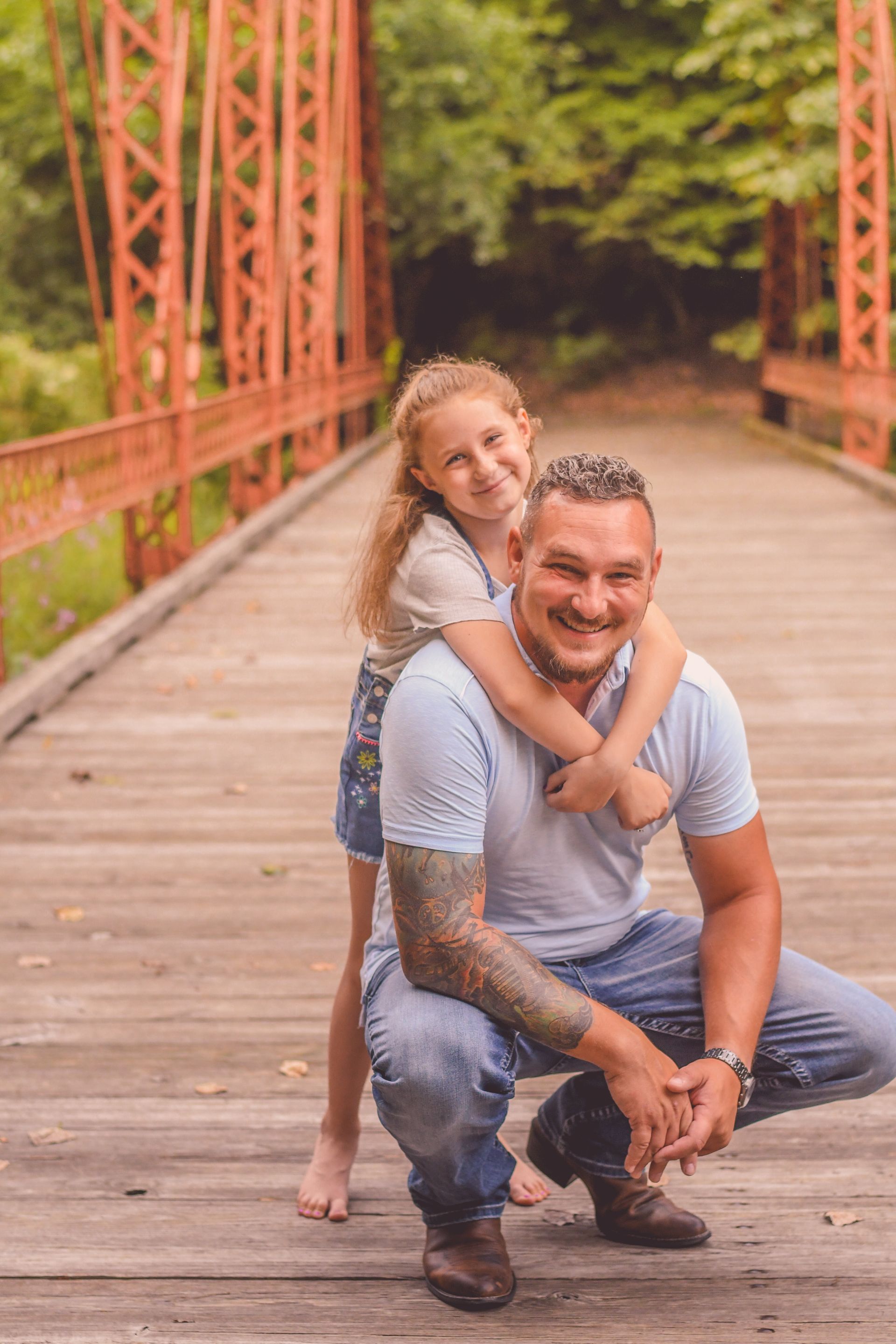 Man crouching on a wooden bridge while a smiling child hugs him from behind