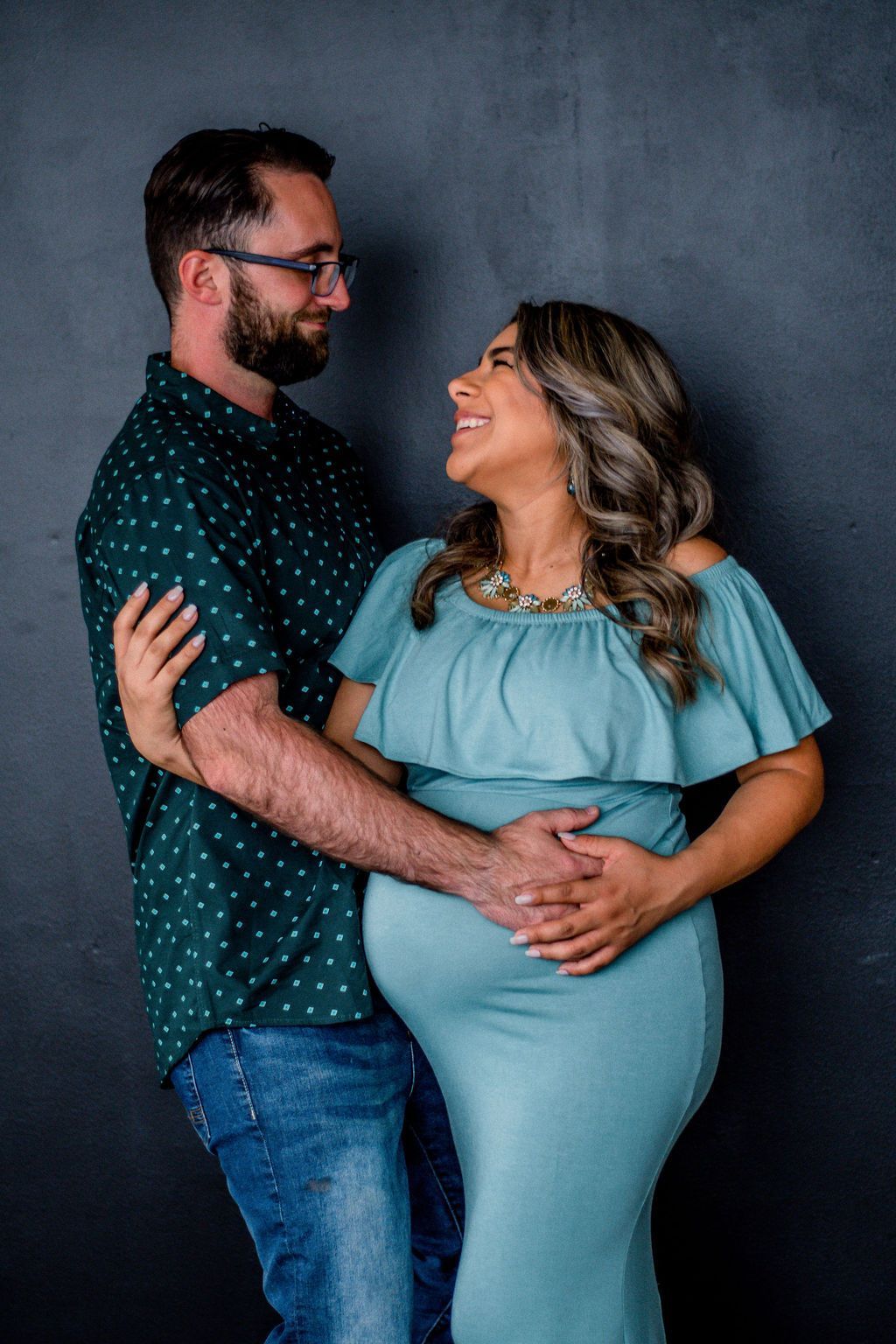 Couple posing together, smiling and embracing against a dark studio backdrop