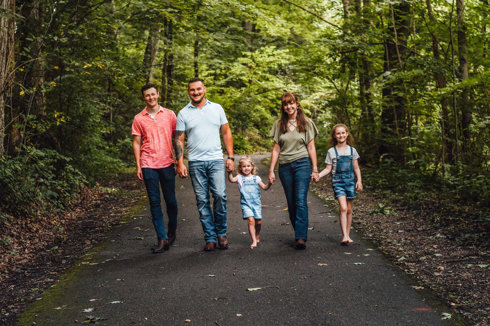 Family walking hand in hand on a forest road, surrounded by green trees