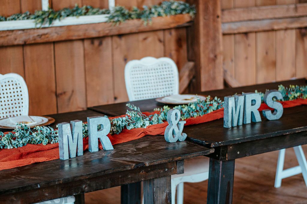 “MR” and “MRS” signs on a decorated table at a wedding reception, with red and green accents