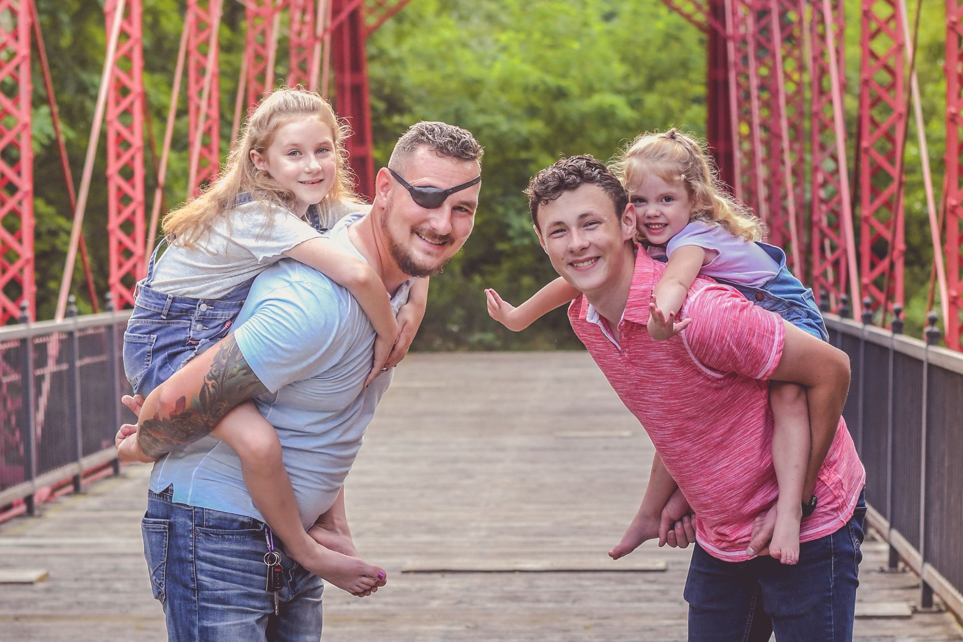 Two people giving piggyback rides on a red bridge, smiling at the camera.