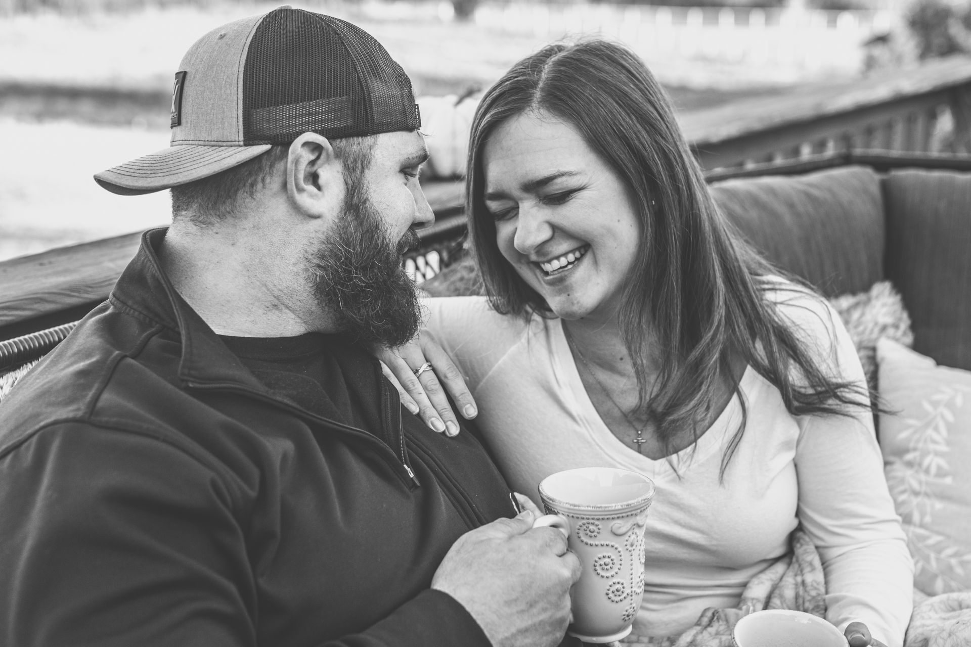 Two people smiling on a couch, sharing coffee outdoors in black and white.