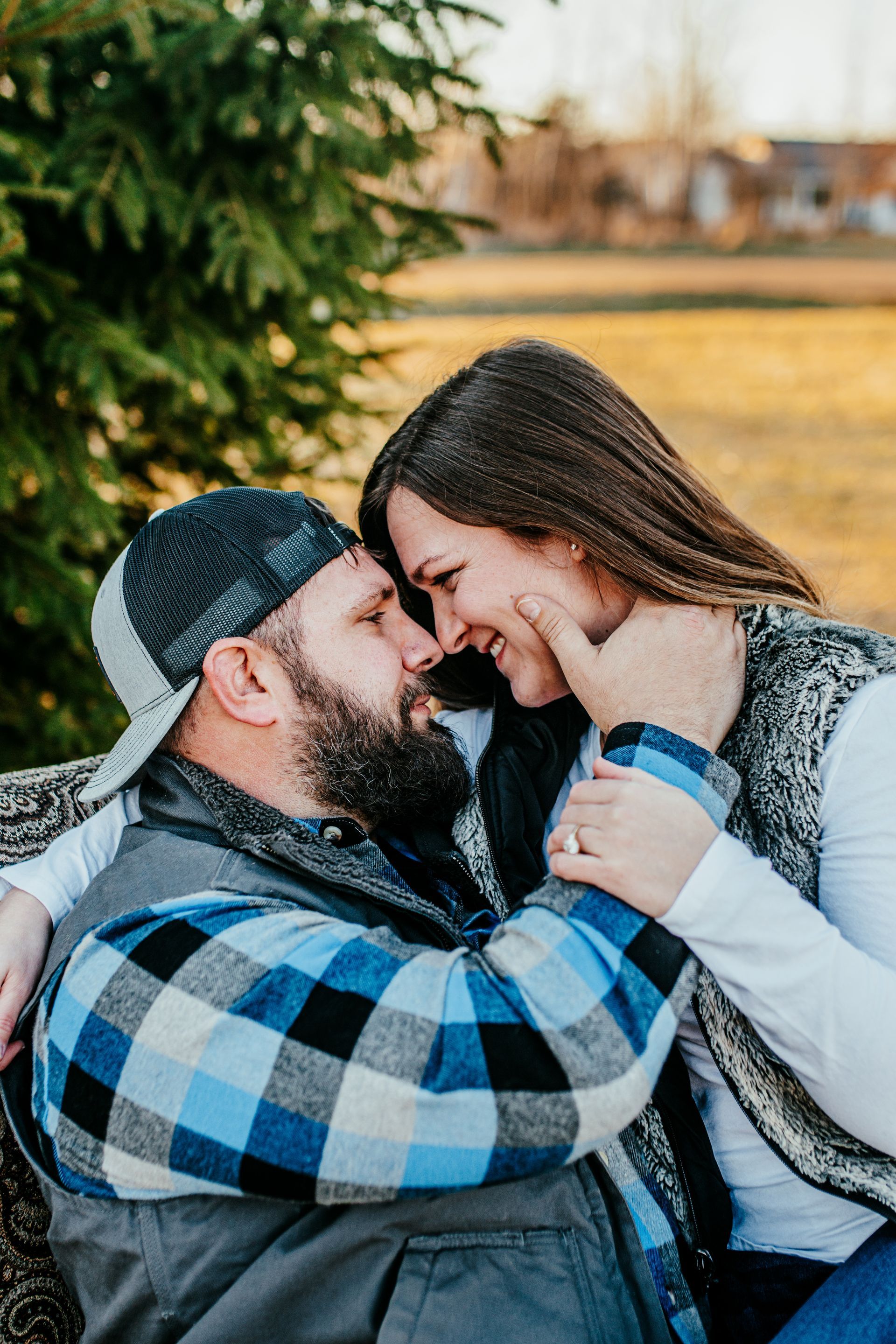 Couple smiling and touching foreheads outdoors in winter, wearing blue and gray plaid and white sweaters