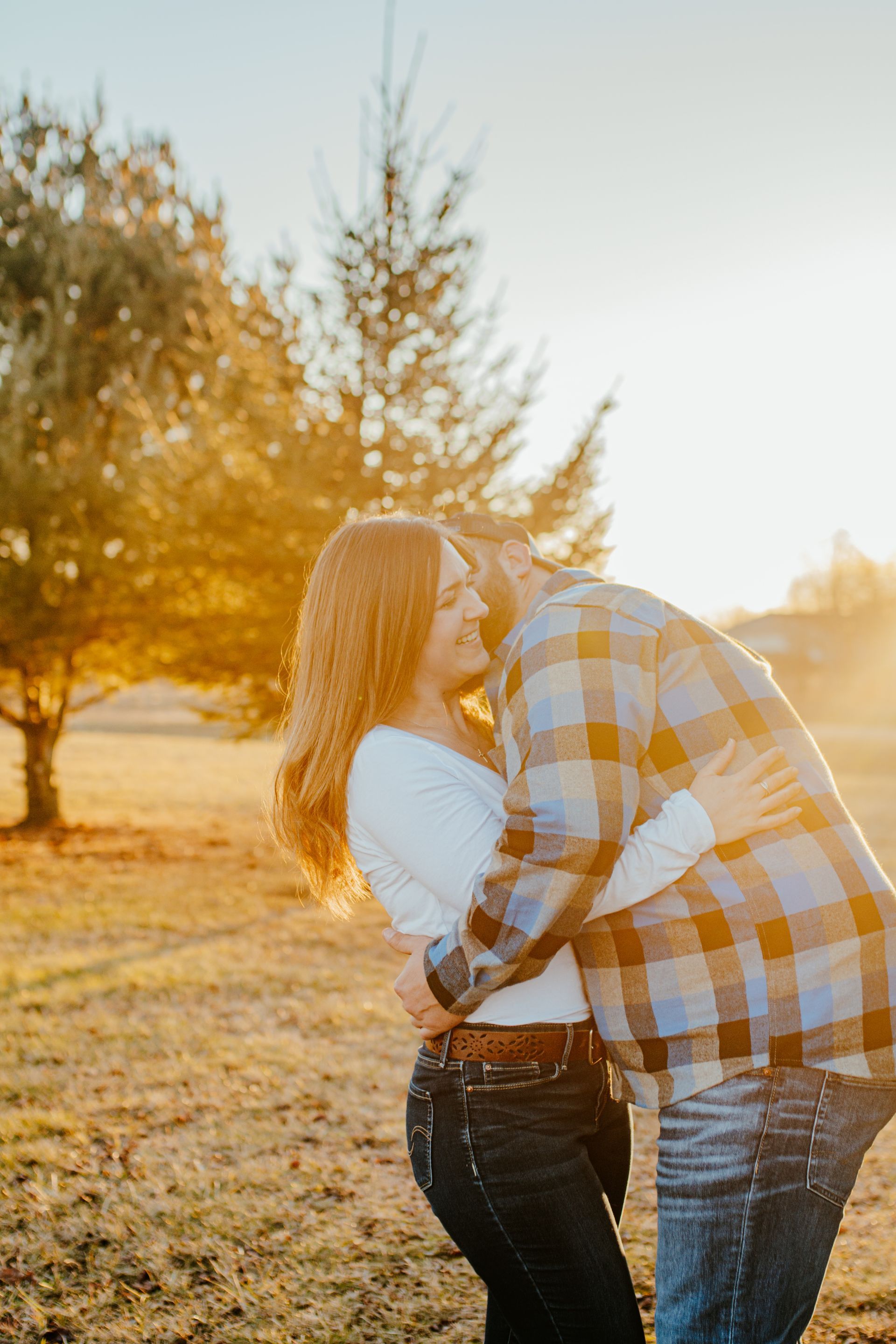 Couple kissing in a sunlit field at sunset, with warm golden light and trees in the background