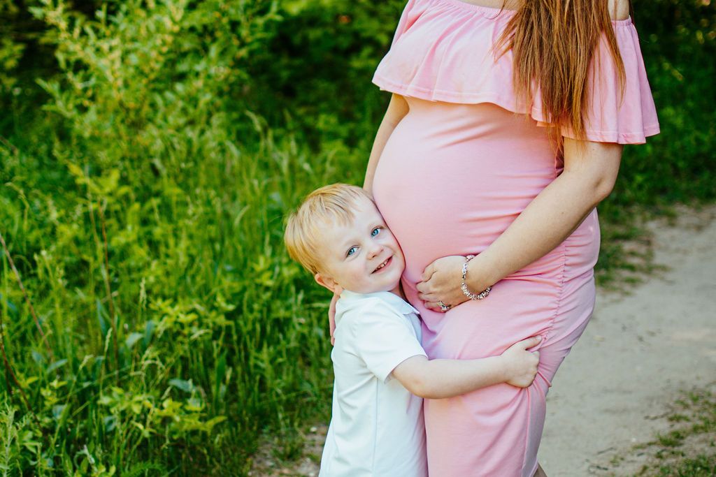 Child hugging a pregnant woman in a pink dress beside a grassy path