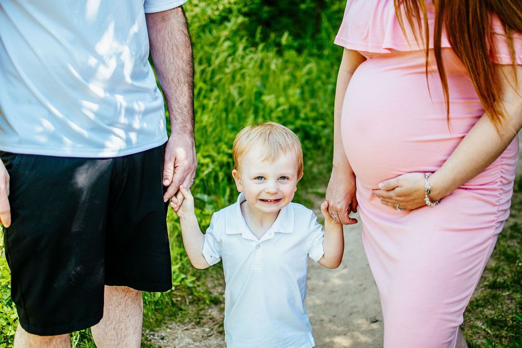Family walking outdoors, smiling child between two adults, one wearing a pink dress and one in a white shirt.