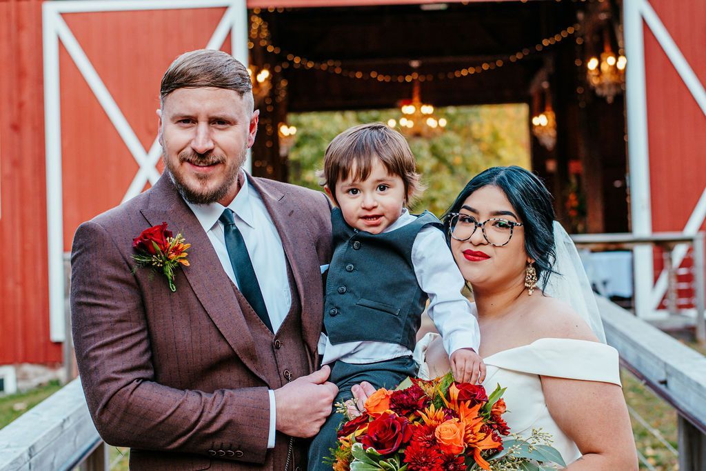 Family portrait in front of a red barn, holding a bouquet of colorful flowers and smiling