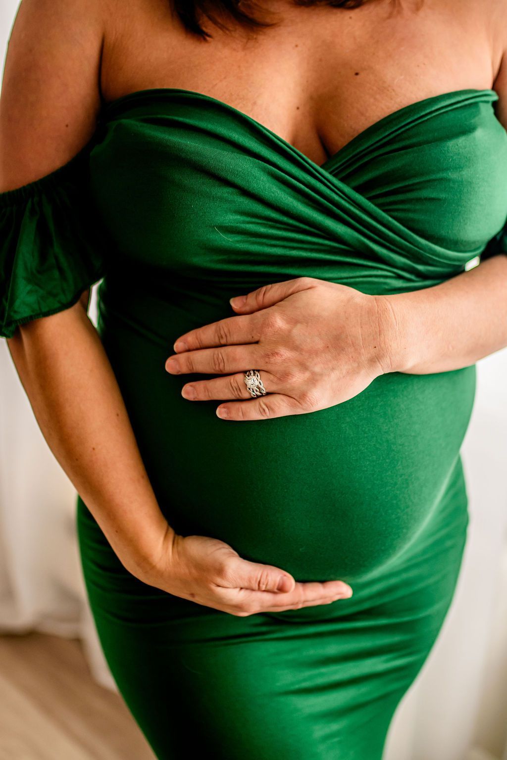 Pregnant person in a green dress gently holding their belly
