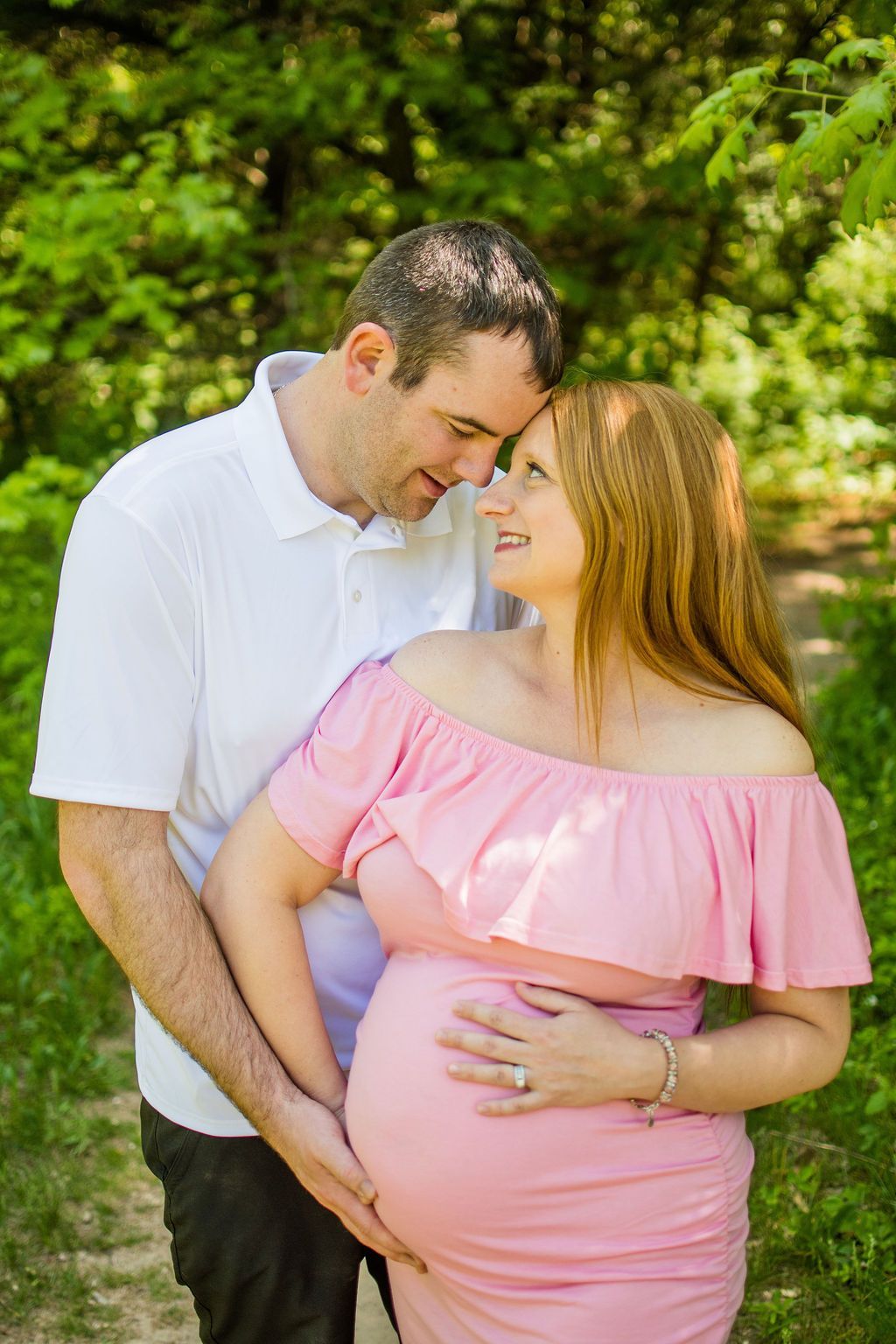Couple embracing outdoors, smiling with forehead touching, in a green garden.
