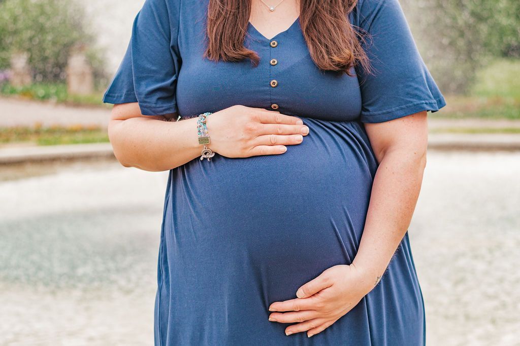 Pregnant person in a blue dress holding their belly outdoors