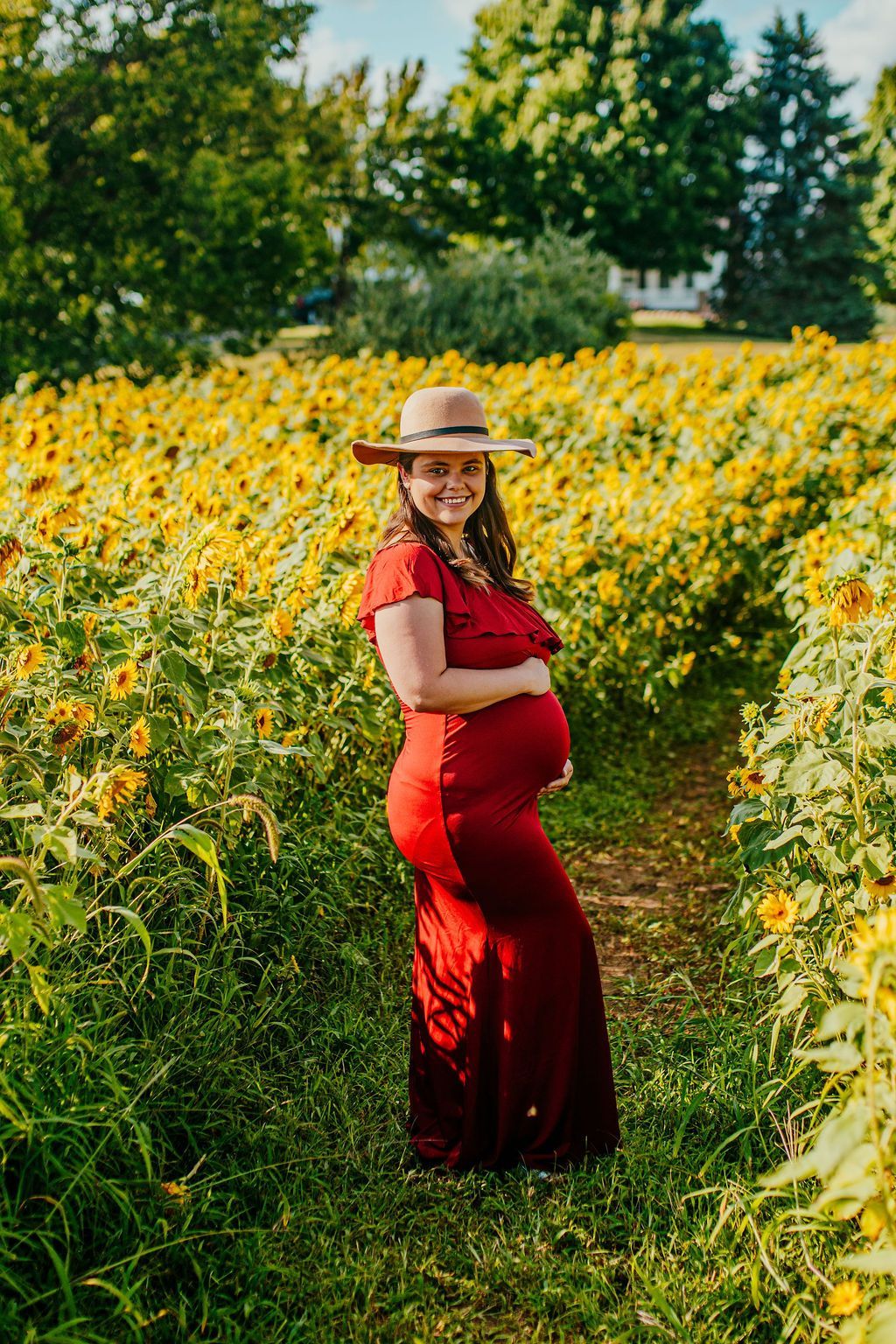 Pregnant woman in a red dress and straw hat standing in a sunflower field