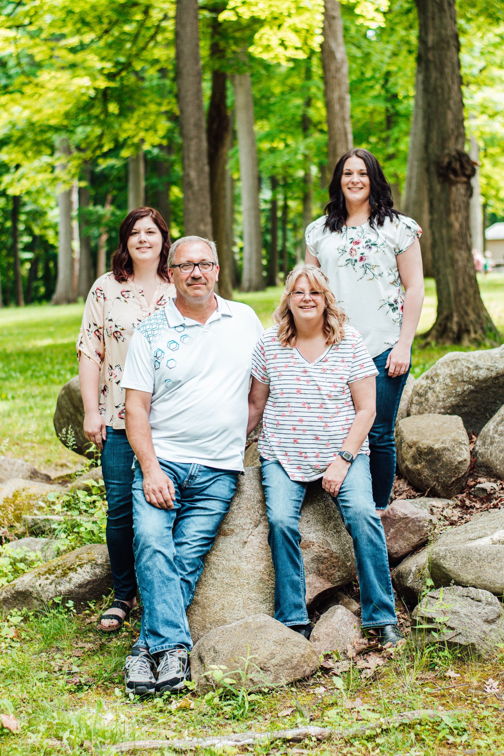 Four people posing on rocks in a green park with trees in the background.