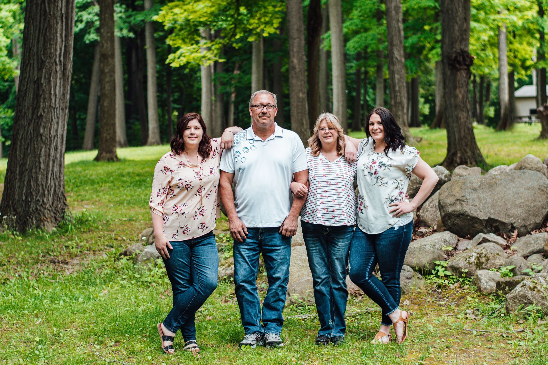 Four adults stand together on grass in a wooded park, smiling at the camera.