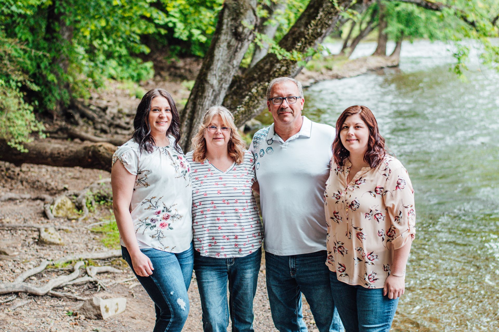 Four people standing outdoors by a creek and trees, smiling at the camera.