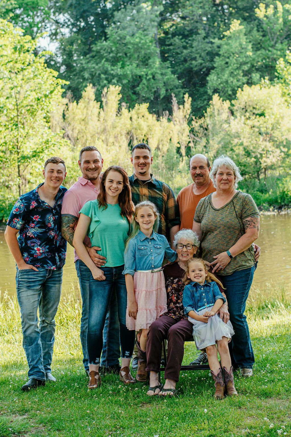 Nine people standing together in a sunlit park, smiling for a family portrait.