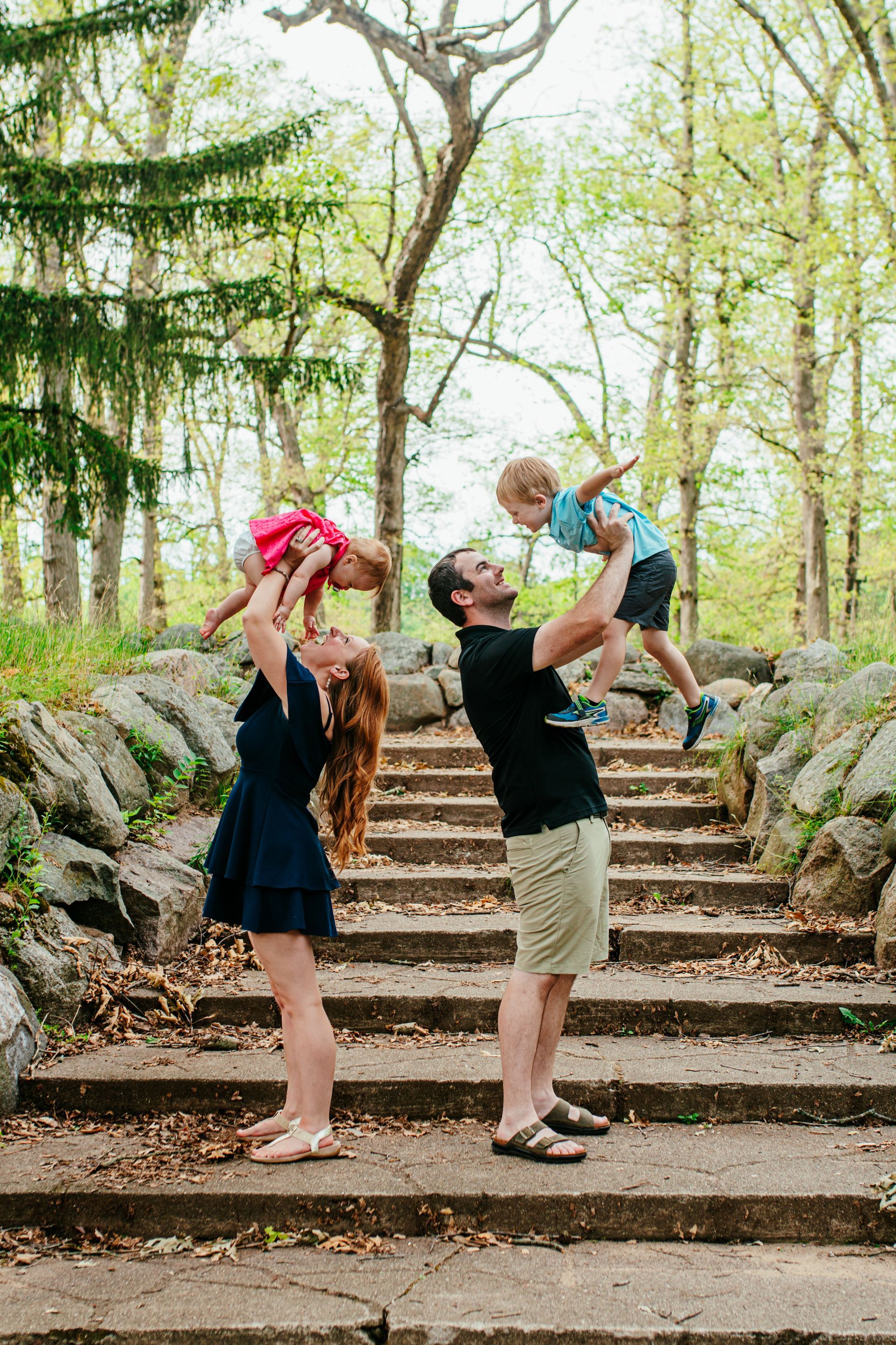 Adult and child lifting toddlers on a stone staircase in a wooded park