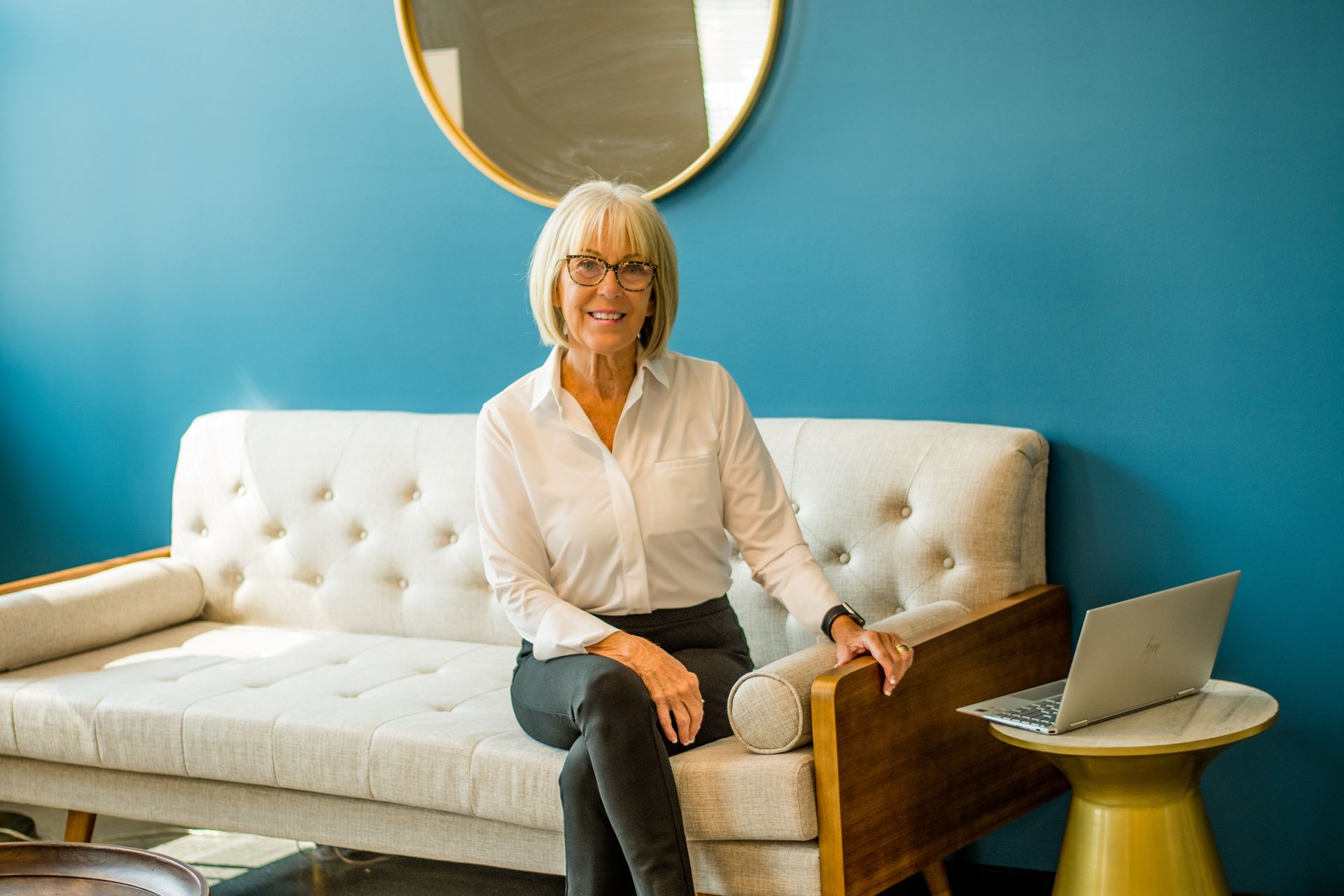 Person seated on a white tufted sofa in a bright room with a blue wall and laptop on a side table