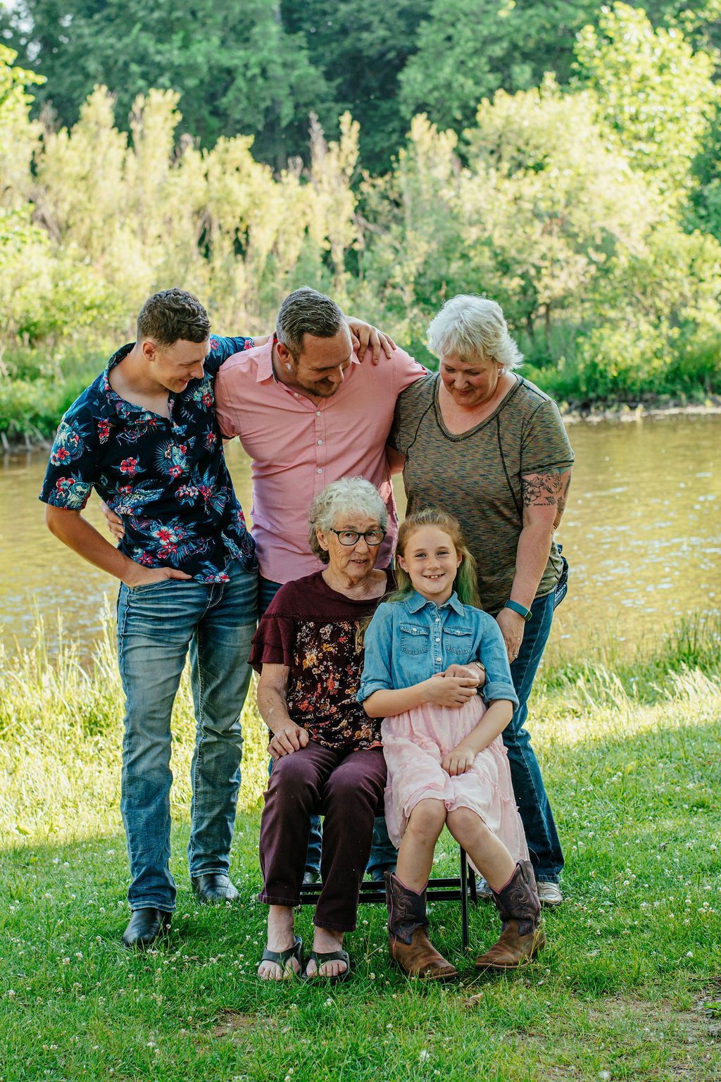 Five people pose together on a grassy lawn by a pond with trees in the background.