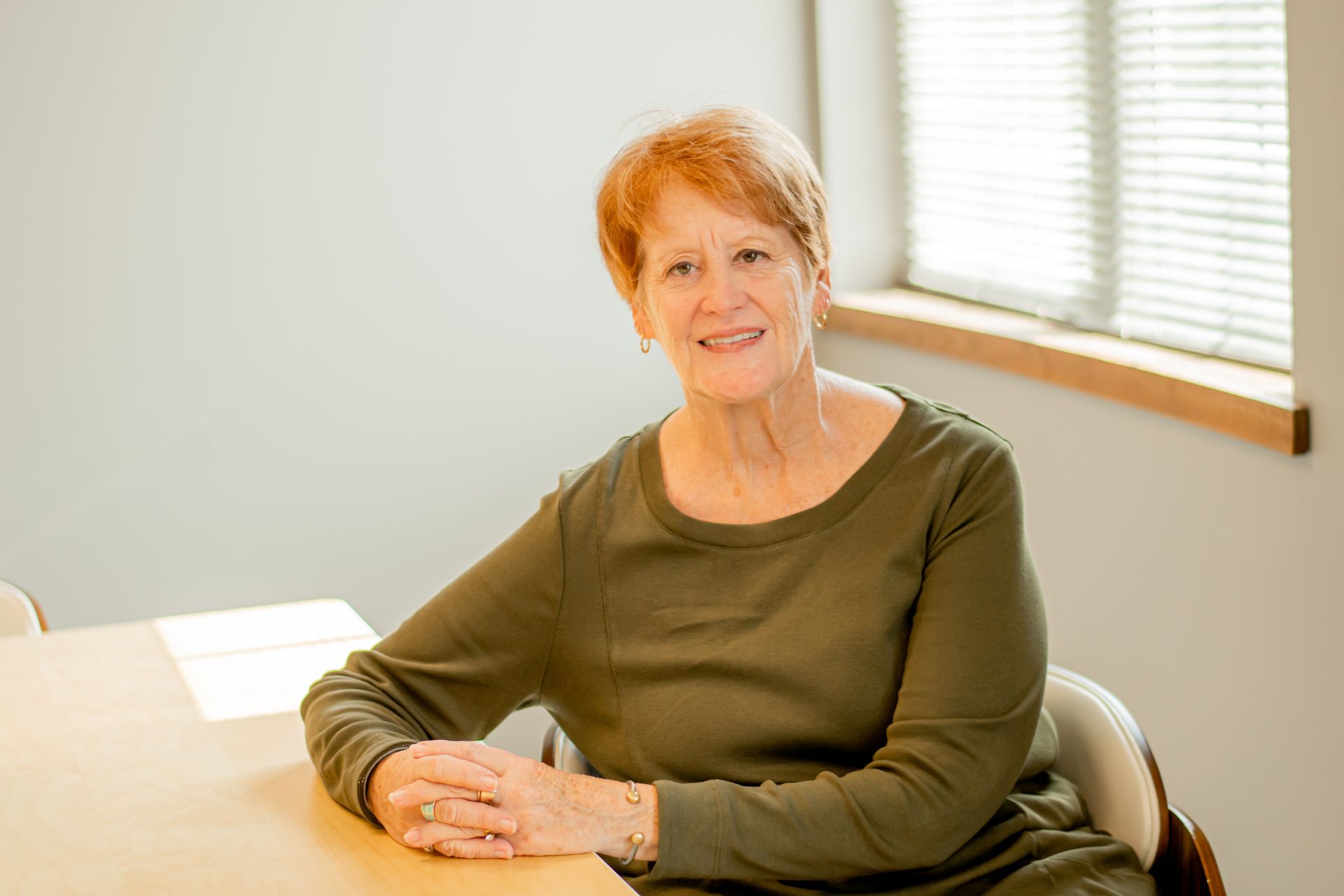Smiling woman sitting at a table in a bright room by a window