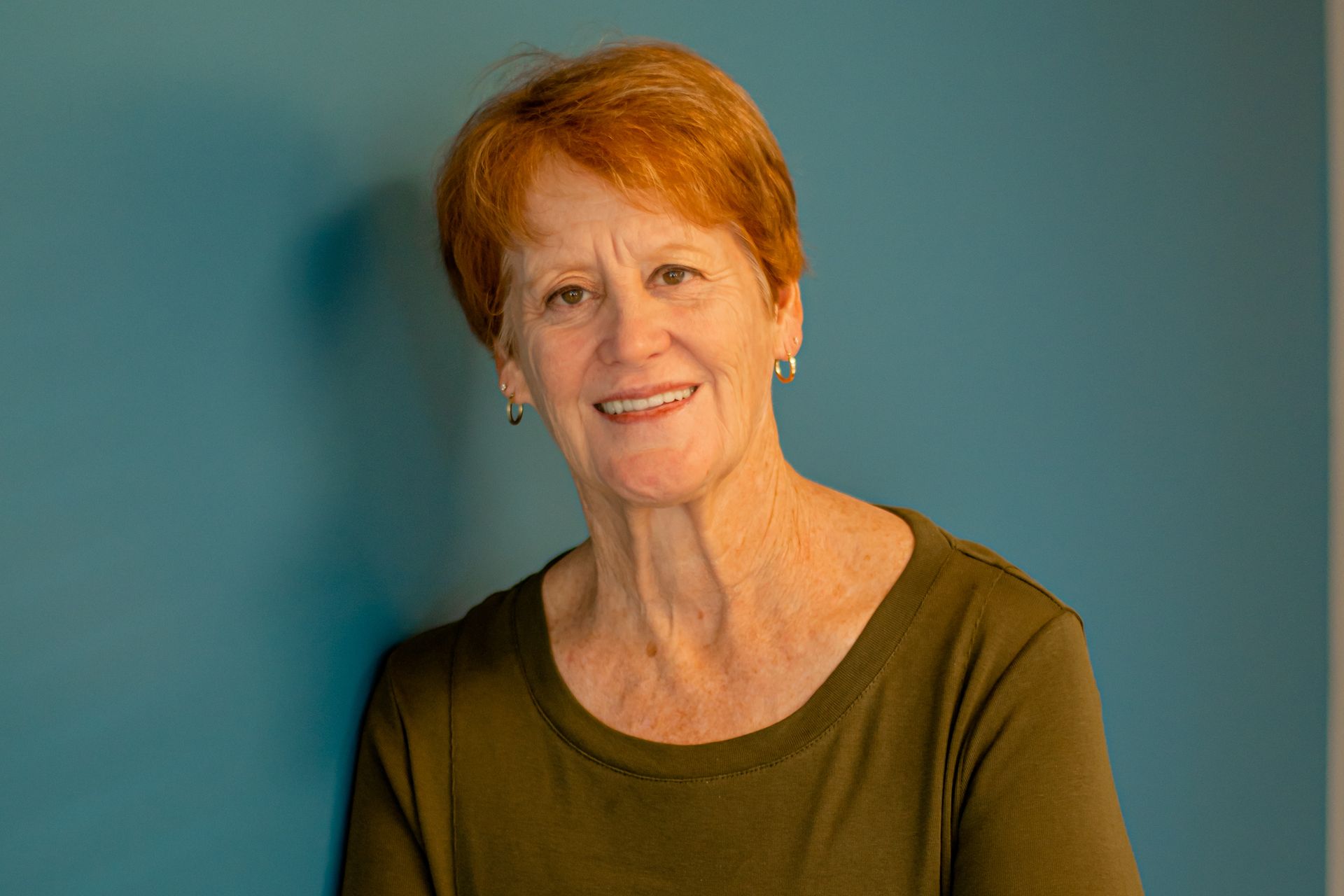 Smiling woman in an olive shirt against a teal wall