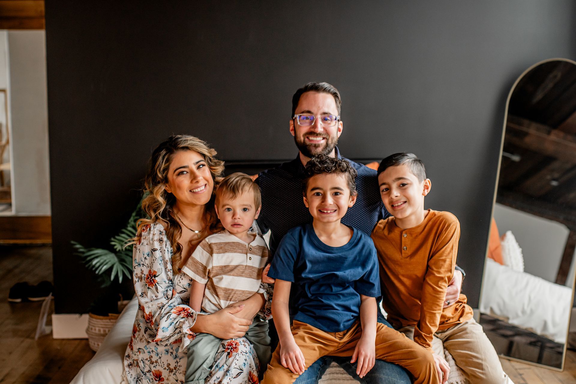 Family of five seated together on a couch in a living room, smiling at the camera.