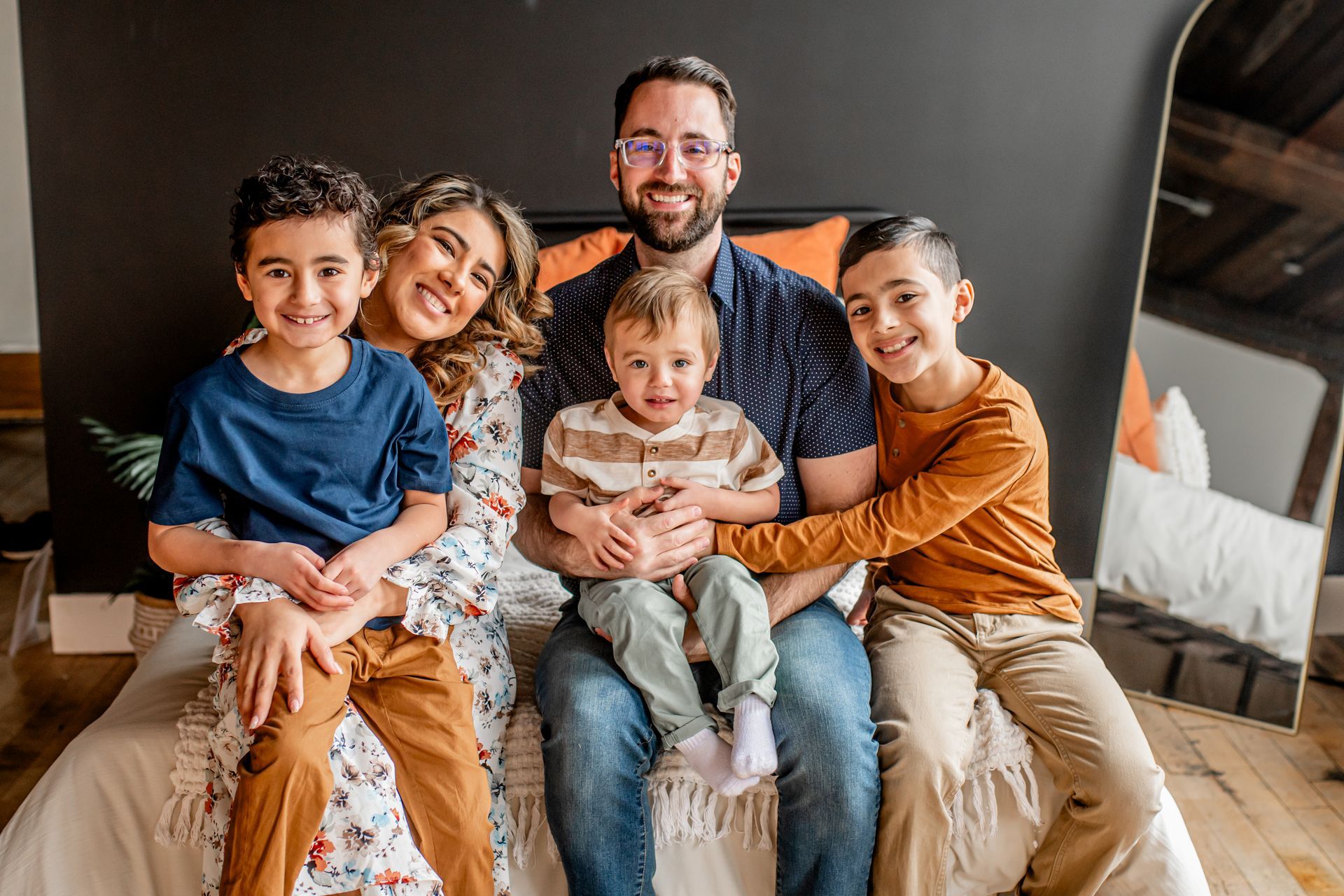 Family of five sitting on a couch, smiling and cuddling in a cozy living room.