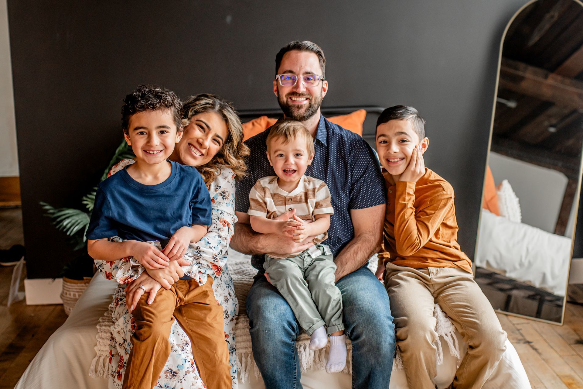 Family of five sitting together on a couch, smiling in a cozy living room.