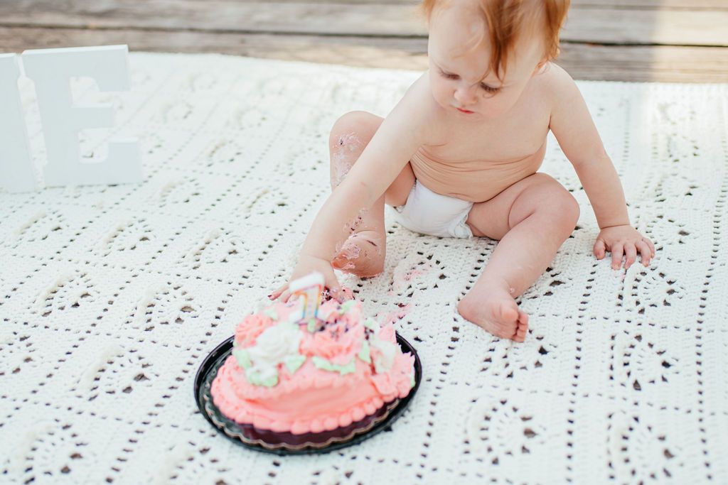 Toddler reaching toward a pink frosted cake on a white lace rug