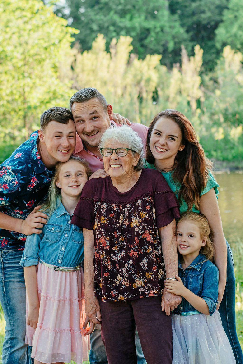 Family group posing outdoors in a green park, smiling and hugging each other.