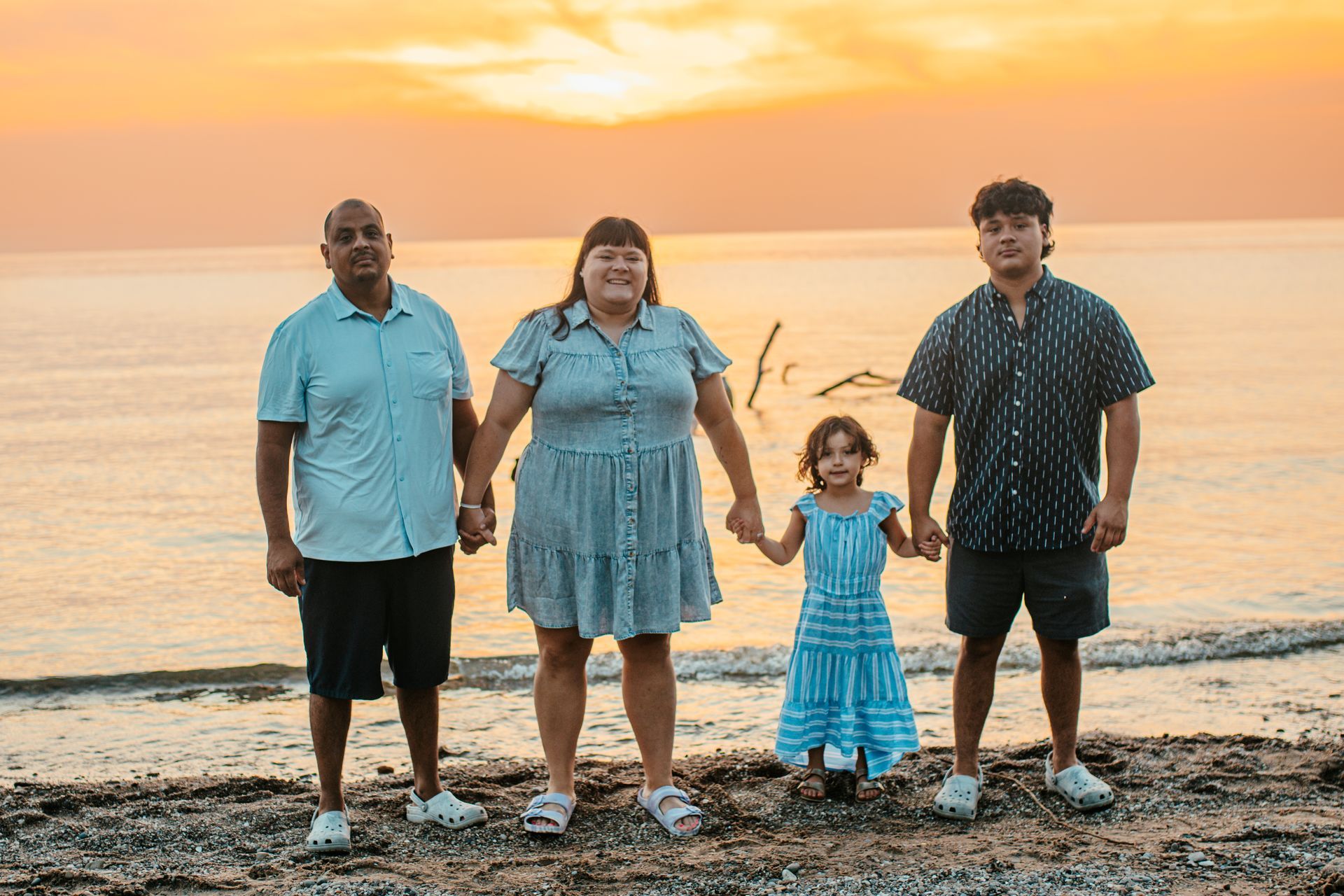 Four people holding hands on a beach at sunset, with the ocean behind them.