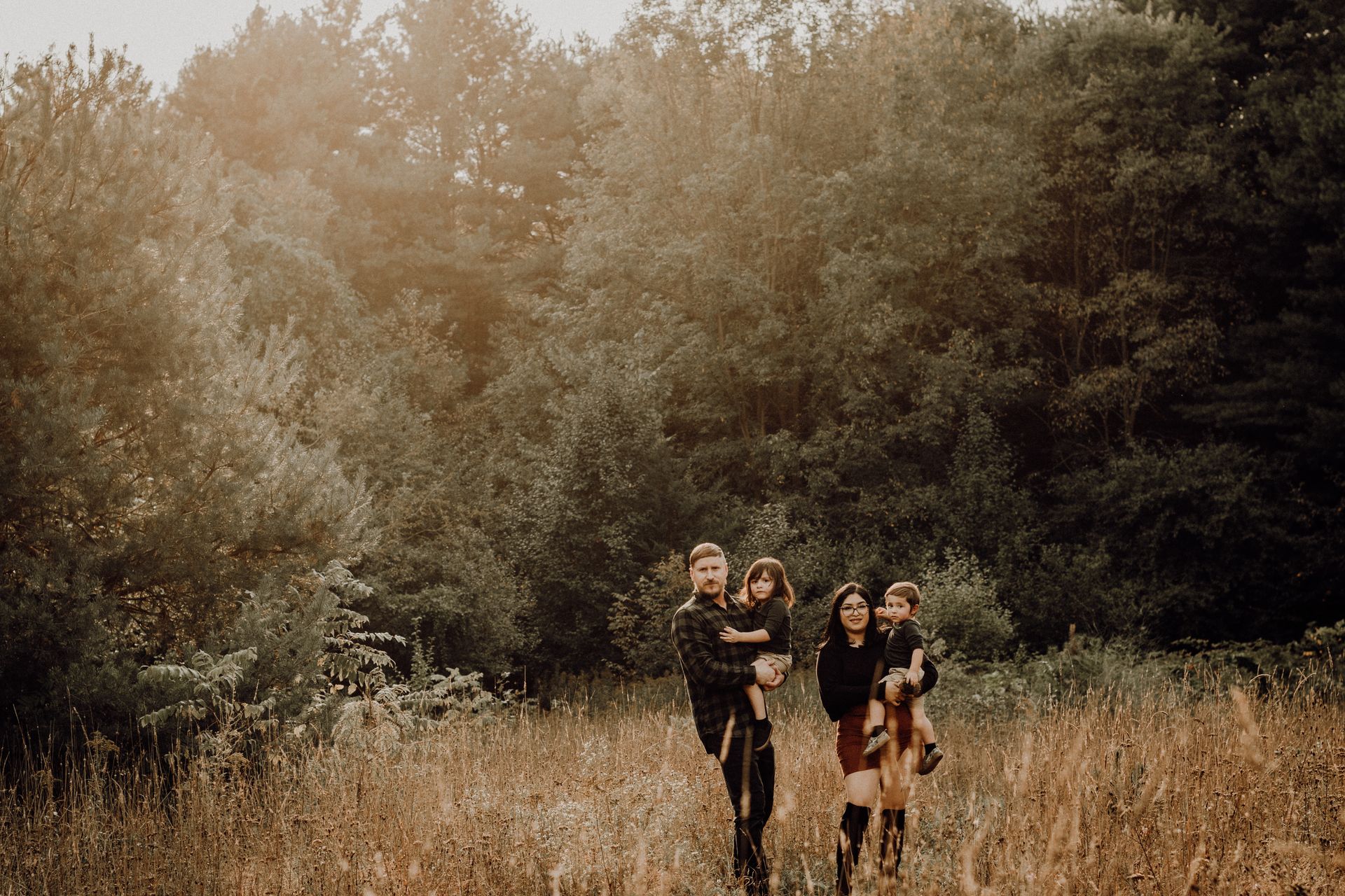 Four people walking through tall grass in a wooded field at sunset