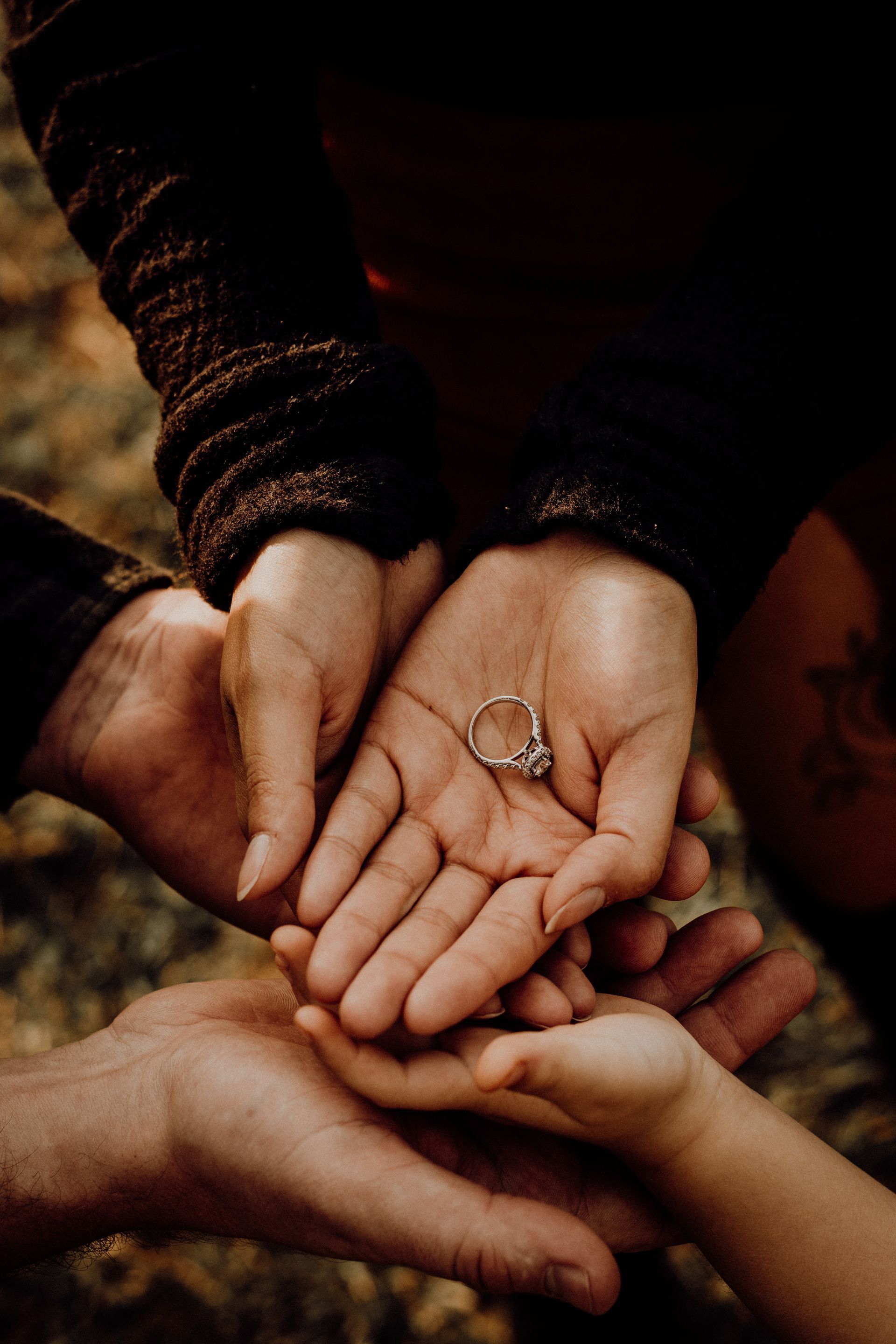 Several hands stacked together, one holding a small ring, in warm low light