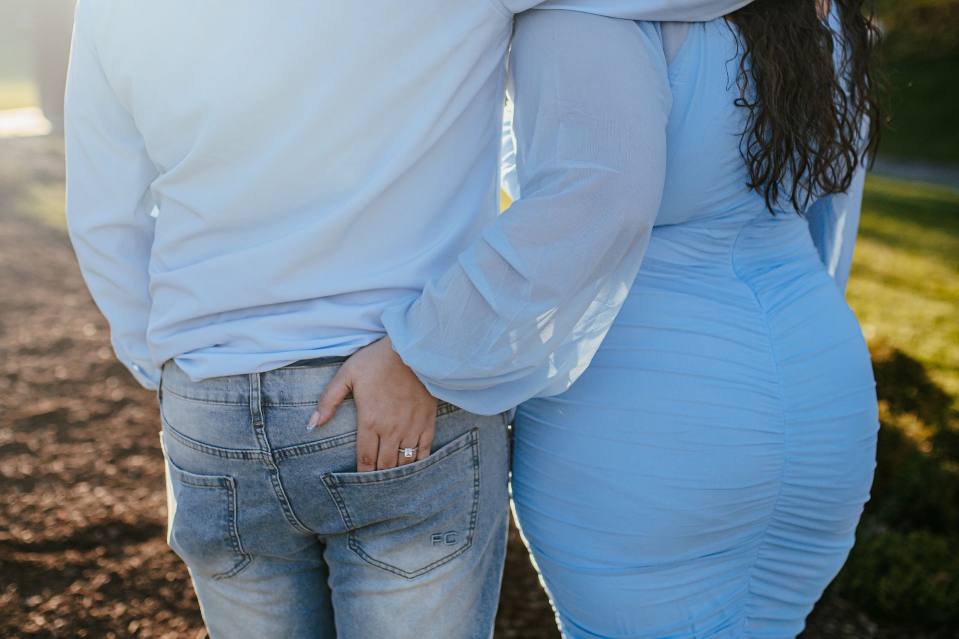 Two people standing close outdoors, one in a white shirt and jeans, the other in a light blue dress.