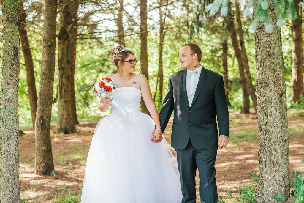 Bride and groom holding hands in a sunlit forest, smiling in wedding attire