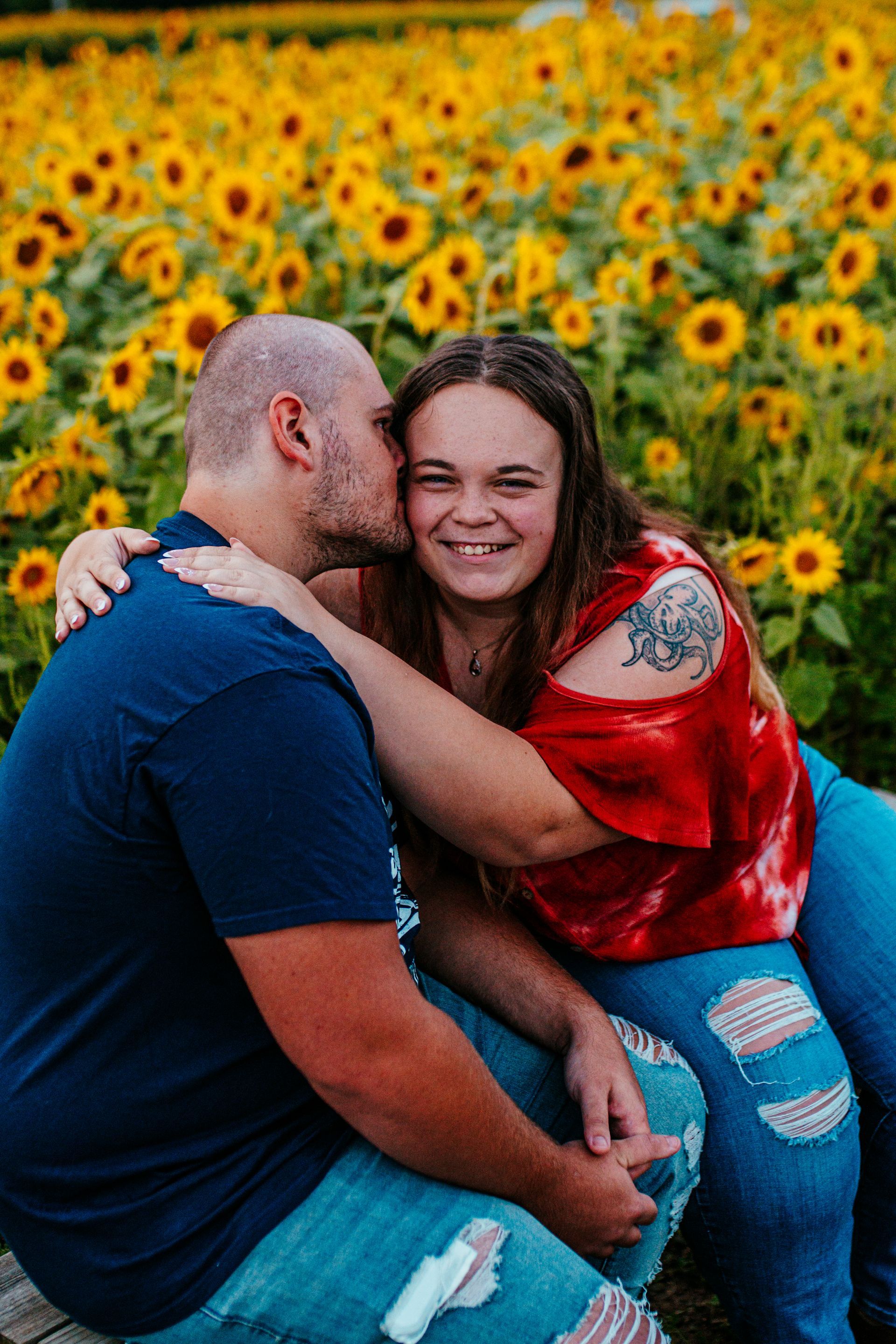 Couple embracing and smiling in a sunflower field, with a vivid blue sky backdrop.