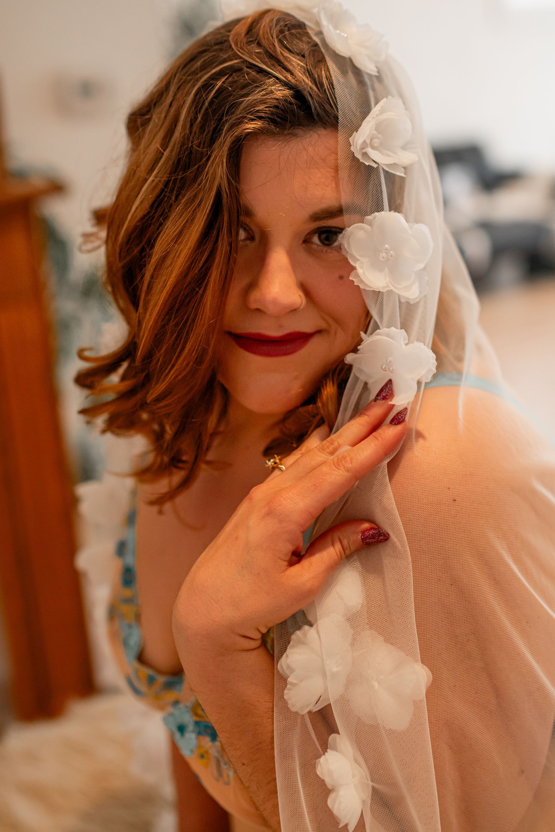 Woman with red hair in a sheer veil, touching her face and smiling softly